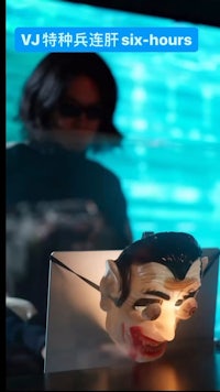 a woman is holding a mask in front of a laptop